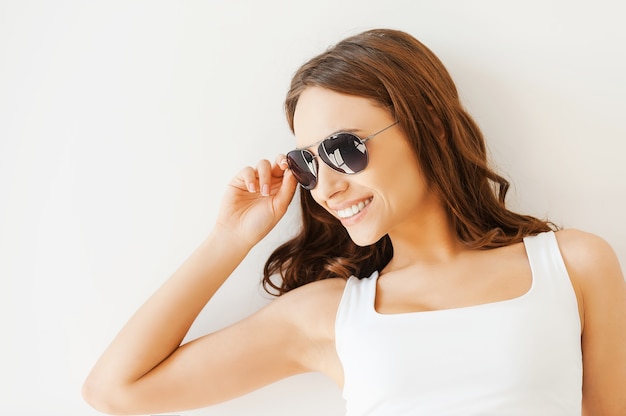 Beleza feliz. Mulher jovem e bonita ajustando os óculos e desviando o olhar em pé contra um fundo branco