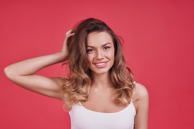 Beleza feminina pura. Mulher jovem e atraente olhando para a câmera e sorrindo em pé contra um fundo rosa