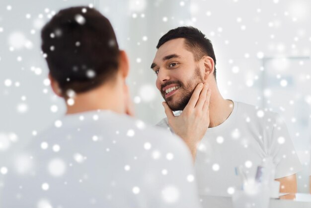 beleza, inverno, natal e conceito de pessoas - jovem sorridente olhando para o espelho no banheiro de casa sobre a neve