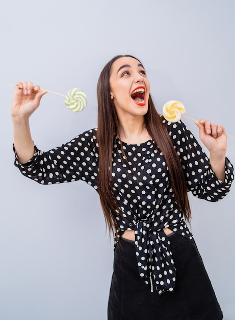 Beleza jovem na camisa pontilhada com dois pirulitos nas mãos. senhora alegre com doces sobre fundo branco.