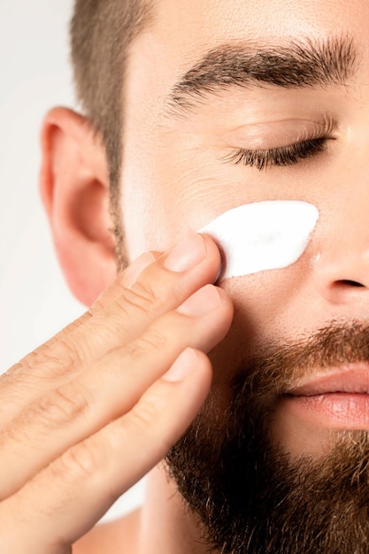 Beleza masculina - jovem está aplicando um creme hidratante e anti-envelhecimento no rosto contra um fundo branco