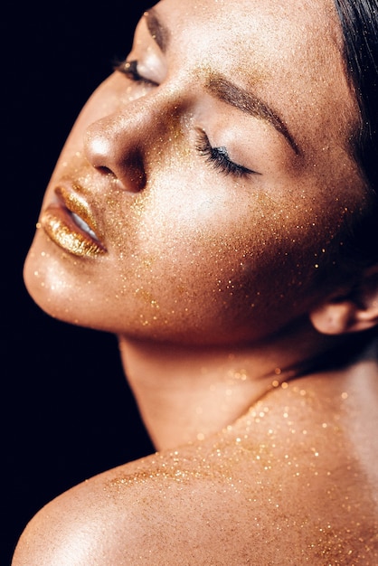 Foto beleza moda arte modelo menina com pele dourada. feche o retrato de uma menina de olhos azuis em fundo preto