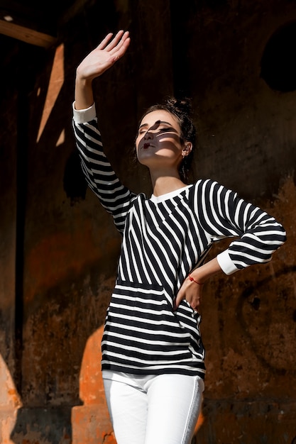 Beleza moda modelo garota com cabelo castanho sobre um fundo de um prédio antigo, abandonado, vestindo roupas elegantes.