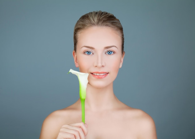 Beleza natural. Mulher saudável com flor de lírio sorrindo sobre fundo azul