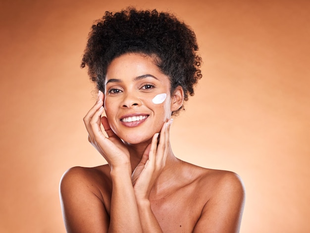 Beleza para a pele e mulher negra com creme facial em estúdio para hidratação em fundo marrom Sorriso de retrato e modelo feminino feliz com creme de loção facial ou produto cosmético para pele saudável