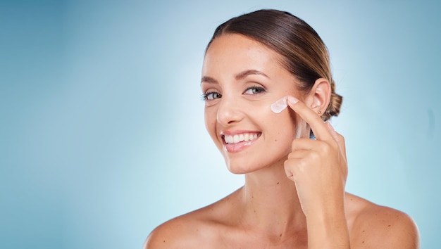 Beleza para a pele e retrato de uma mulher com creme facial para saúde, bem-estar e rotina facial natural Cosmético feliz e modelo com loção facial spf ou creme isolado por um fundo azul do estúdio