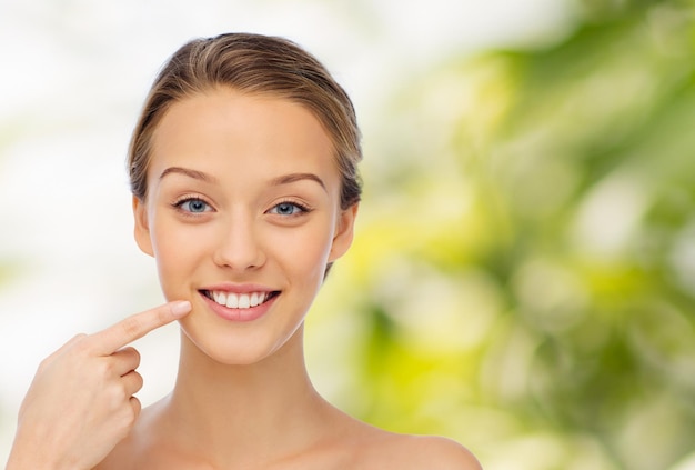 beleza, pessoas, cuidados dentários e conceito de higiene - jovem feliz apontando o dedo para o sorriso ou dentes sobre fundo verde natural