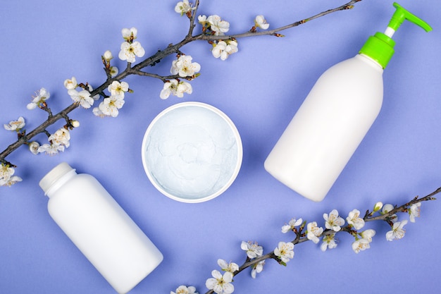 Beleza primavera cosméticos naturais, creme com ramos de flores sobre fundo violeta.