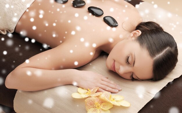 beleza, saúde, férias, pessoas e conceito de spa - linda mulher no salão de spa recebendo massagem com pedras quentes