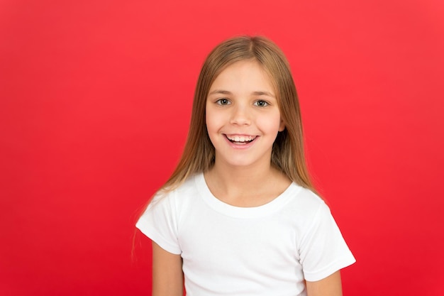 Beleza sorridente. Conceito de sorriso brilhante. Menina feliz rosto sorridente sobre fundo vermelho. Rosto sorridente fofo de criança emocional. Emoção sincera. Menina adorável alegre sorrindo. Positivo e otimista.