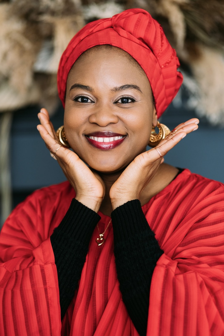 Foto beleza tradicional africana. mulher bonita e alegre em um vestido vermelho, lenço na cabeça e joias posando contra o fundo do estúdio e olhando para a câmera.