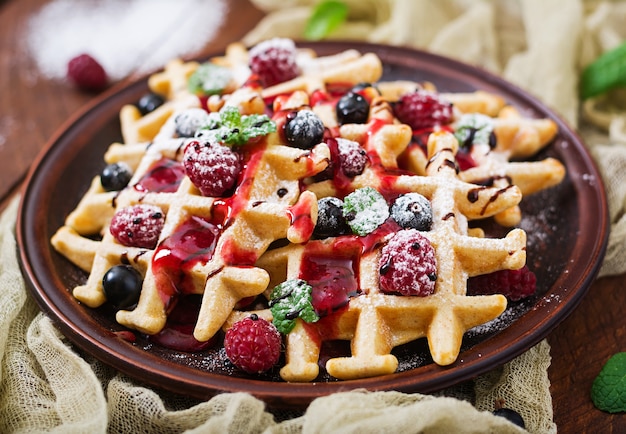 Foto bélgica waffles con frambuesas, chocolate y jarabe en un plato.