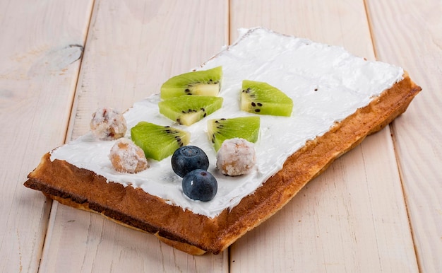 Belgische Waffel mit Creme-Kiwi und Heidelbeeren auf hellem Holzhintergrund