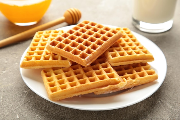 Belgische Waffeln auf grauem Hintergrund. Belgische Waffeln mit Honig und Milch. Frisch gebackene belgische Waffeln.