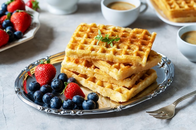 Belgische Waffeln mit Beeren auf Silberteller, Blaubeeren, Erdbeeren, zwei Tassen Kaffee