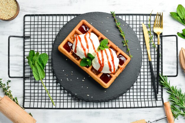 Belgische Waffeln mit Eis, Erdbeermarmelade und Minze Dessert auf einer schwarzen Steinplatte