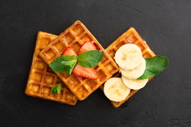 Belgische Waffeln mit Erdbeerbanane und Minze auf schwarzem Steinhintergrund