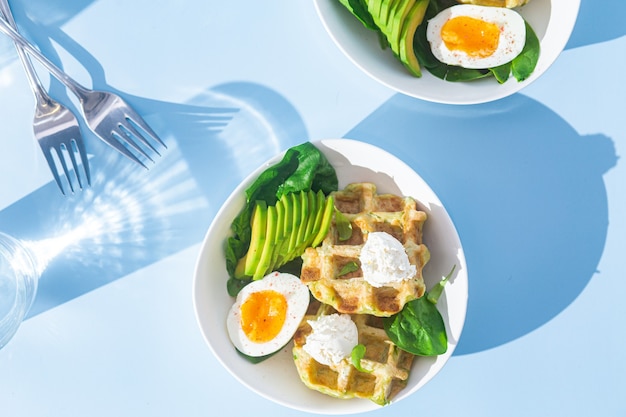 Belgische Waffeln mit Frischkäse-Ei und Avocado in einem weißen Teller Gesundes Frühstück