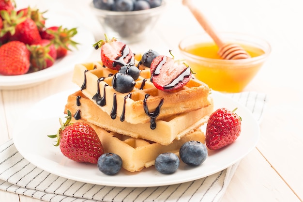 Belgische Waffeln mit Honig, Schokolade, Erdbeere, Blaubeere, Ahornsirup und Sahne.