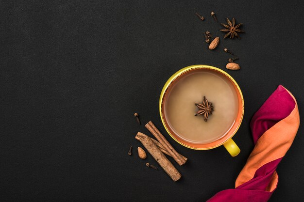 Beliebte asiatische Erwärmung trinken Masala-Tee in einer gelben Tasse mit Koriander, Zimt und Rosenstiel auf einem schwarzen Hintergrund.