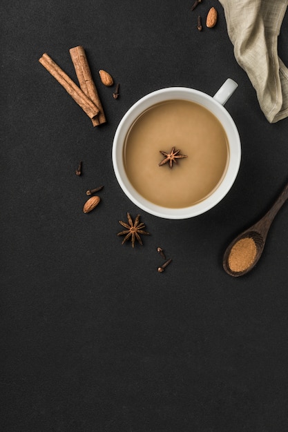 Beliebte asiatische Erwärmung trinken Masala-Tee in einer weißen Tasse mit Koriander, Zimt und Rosenstiel auf einem schwarzen Hintergrund.