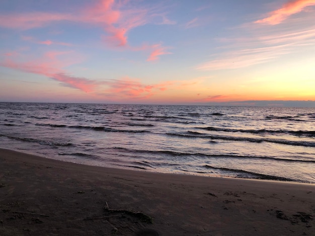 Foto belíssima paisagem marítima com ondas praia de areia vazia pôr do sol azul rosa céu amarelo águas rasas