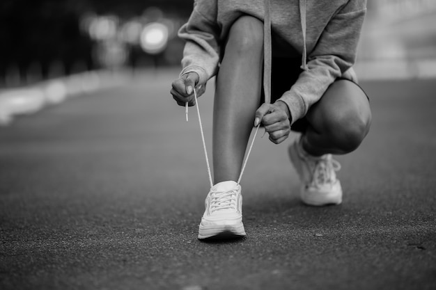 bella atleta sentada atándose los cordones de los zapatos en zapatillas blancas foto en blanco y negro