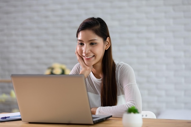 Bella atractiva mujer india asiática trabajando con computadora portátil y pensando en obtener ideas y requisitos en el inicio del negocio en casa sintiendo tan felicidadConcepto de inicio del negocio