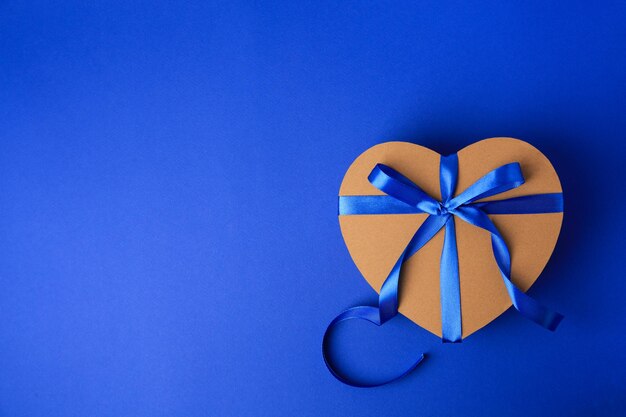Bella caja de regalo en forma de corazón con arco en fondo azul vista superior Espacio para texto