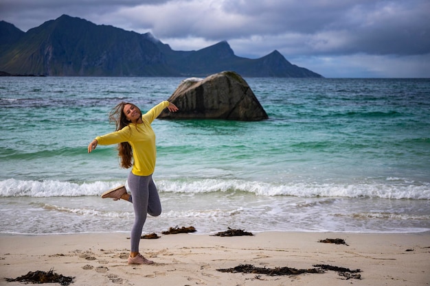 bella chica de pelo largo levanta las manos en el aire en la famosa playa paradisíaca de haukland, noruega