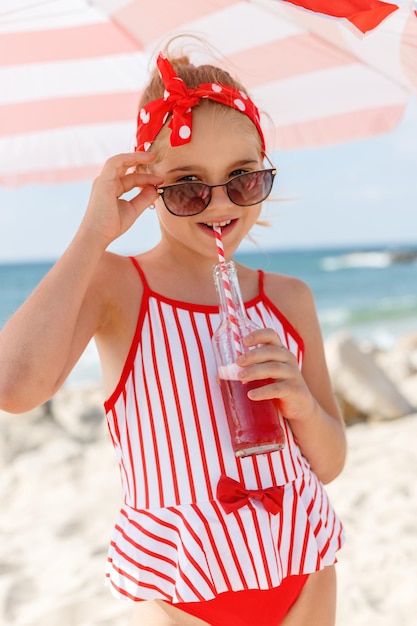 Bella chica en un traje de baño rojo con una botella de sidra en la playa al estilo pinup