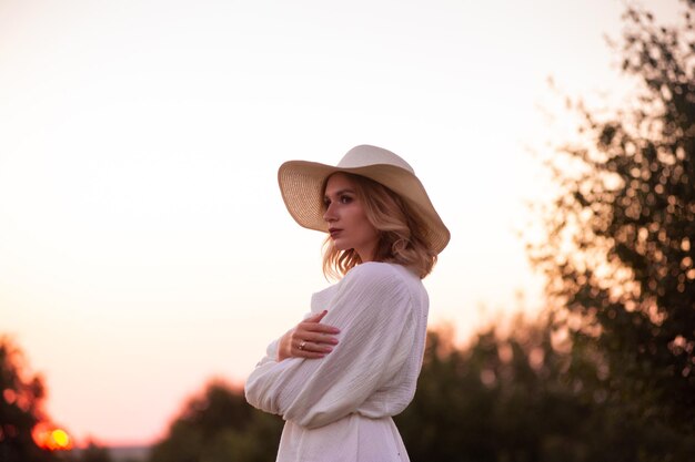 bella chica con vestido blanco y sombrero en un campo de lavanda al atardecer