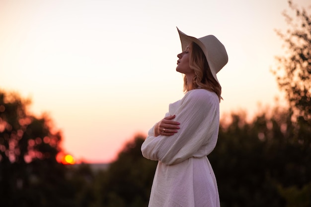 Foto bella chica con vestido blanco y sombrero en un campo de lavanda al atardecer