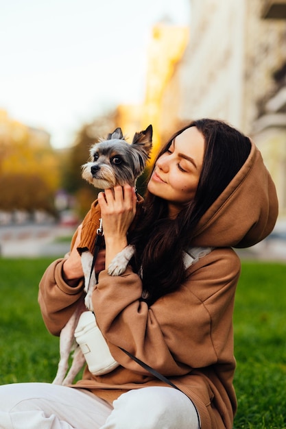 bella dama con ropa informal sentada en el césped con un lindo perrito en los brazos