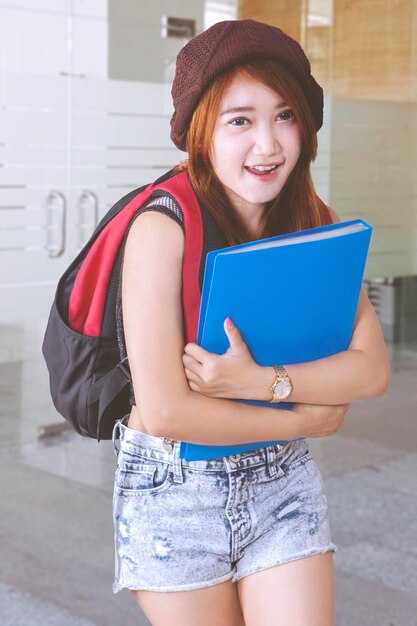 Bella estudiante asiática llevando una mochila y una carpeta sonriendo a la cámara