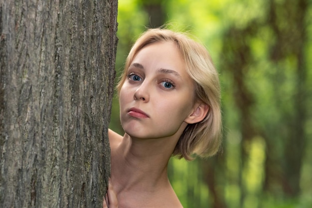 Bella joven al lado del árbol en el bosque