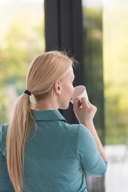 bella joven bebiendo café matutino junto a la ventana de su casa