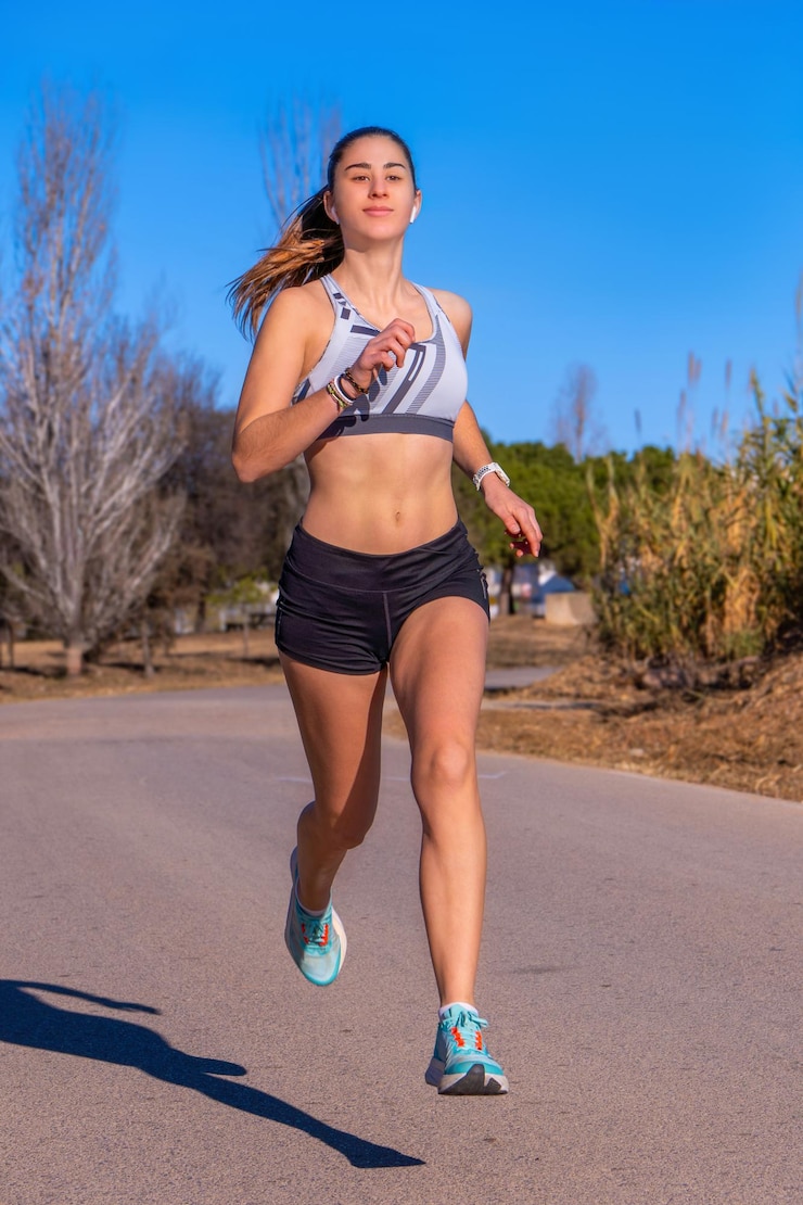 Foto bella joven corredora bronceada vestida con pantalones cortos y camiseta blanca corriendo suspendida en el aire