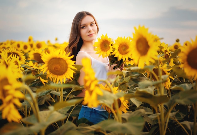 Bella joven delgada con cabello largo en un campo con girasoles en flor al atardecer