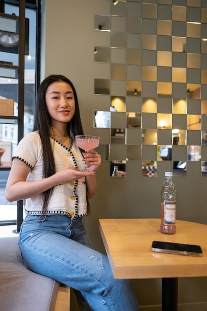 Bella joven elegante con una bebida en la mano sentada en el banco en la mesa del café