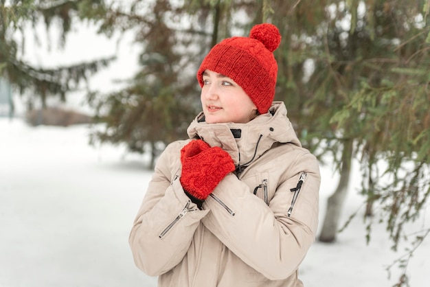 Bella joven con un elegante conjunto de sombreros y guantes rojos de punto en el fondo de un bosque o parque de invierno Caminata de invierno