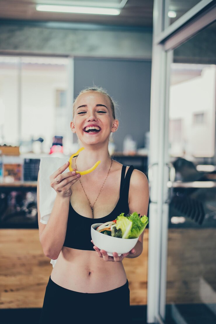 Bella joven con ensalada en el gimnasio. Las mujeres deportivas hacen ejercicio con alimentos saludables. Salud y bienestar mental.