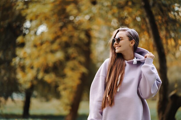 Foto bella joven feliz y sonriente con capucha rosa caminando en la temporada de otoño en el parque