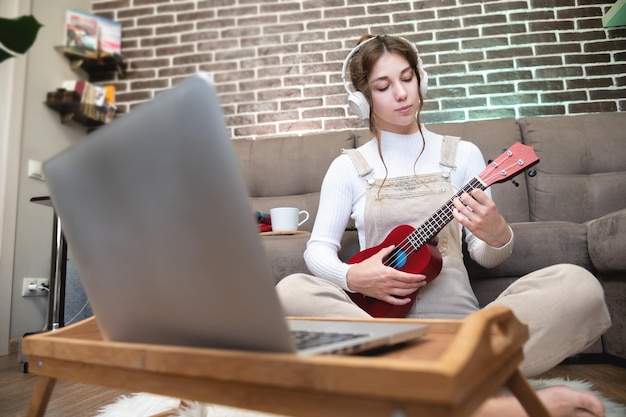 Bella joven hipster en ropa casual aprendiendo a tocar el ukulele mientras está sentada en