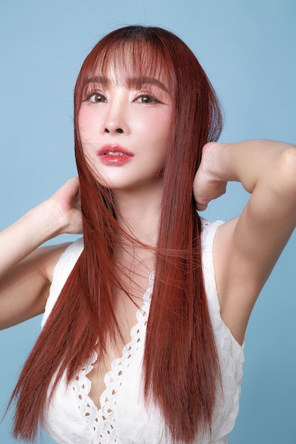 Bella joven modelo asiática de cabello largo con maquillaje natural en la cara piel limpia y fresca en fondo azul aislado retrato de chica linda tratamiento facial cuidado corporal belleza y spa