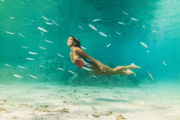 Una bella joven nada bajo el agua disfrutando del azul del mar.