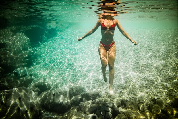 Una bella joven nada bajo el agua disfrutando del azul del mar.