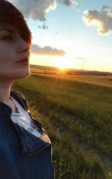 Foto bella joven de pie en el campo durante la puesta de sol