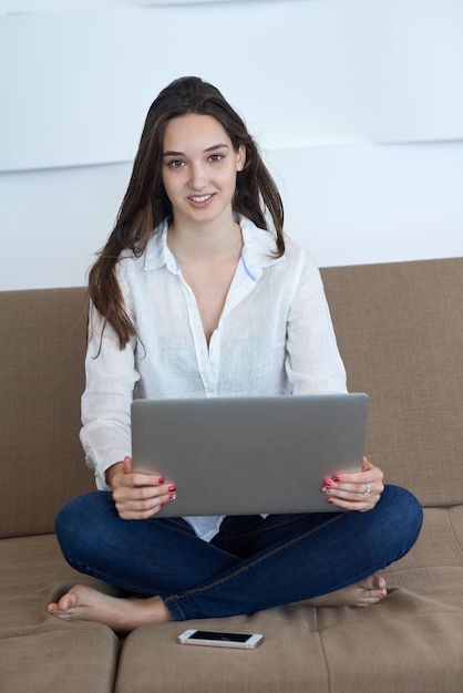 bella joven se relaja y trabaja en una computadora portátil moderna oficina en casa mientras escucha música con auriculares blancos