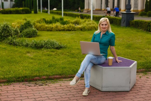 bella joven rubia con una laptop en el parque en un cálido día de verano